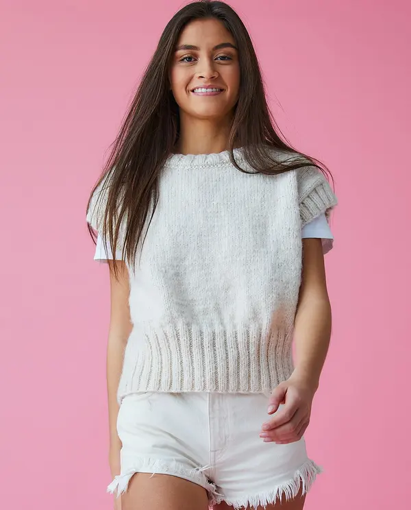 Jovem com colete de malha branco e calções de ganga brancos com fundo rosa