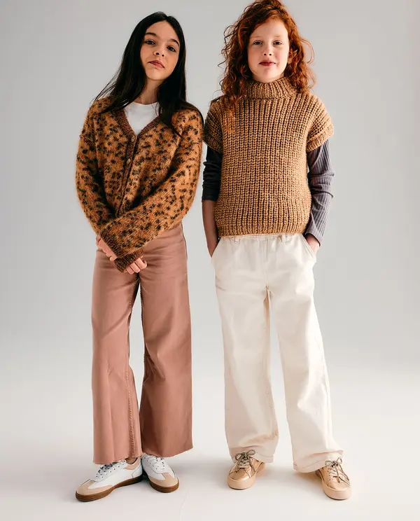 Duas crianças vestidas com roupas casuais de outono em fundo neutro.