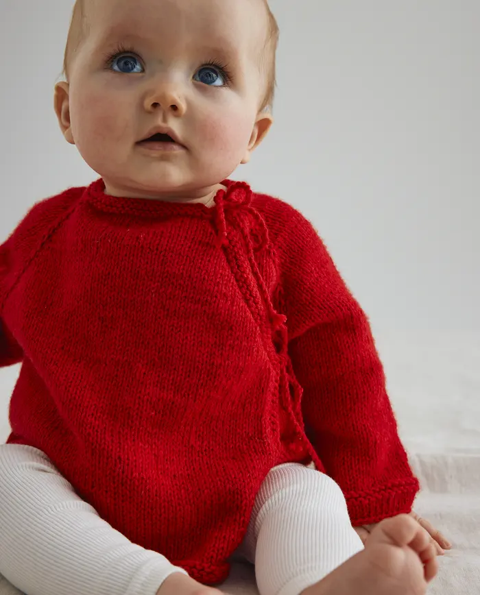 Bebé com camisola vermelha de malha e calças brancas sentado
