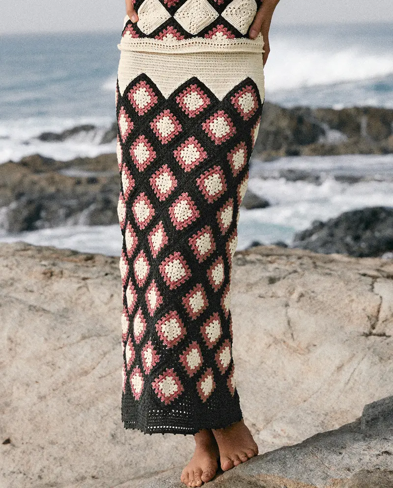 Saia longa de crochet com padrão de losangos creme, preto e rosa junto ao mar