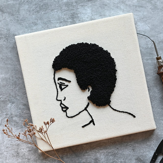 quadro bordado de perfil de mulher com cabelo cacheado preto sobre fundo bege