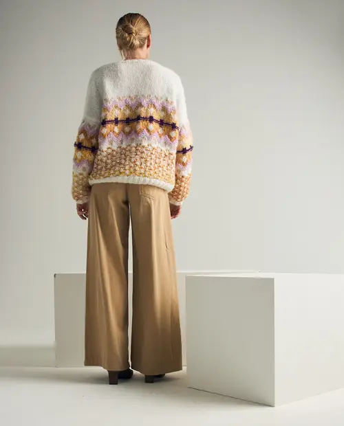 Mulher de costas com casaco de malha e calças largas em fundo minimalista