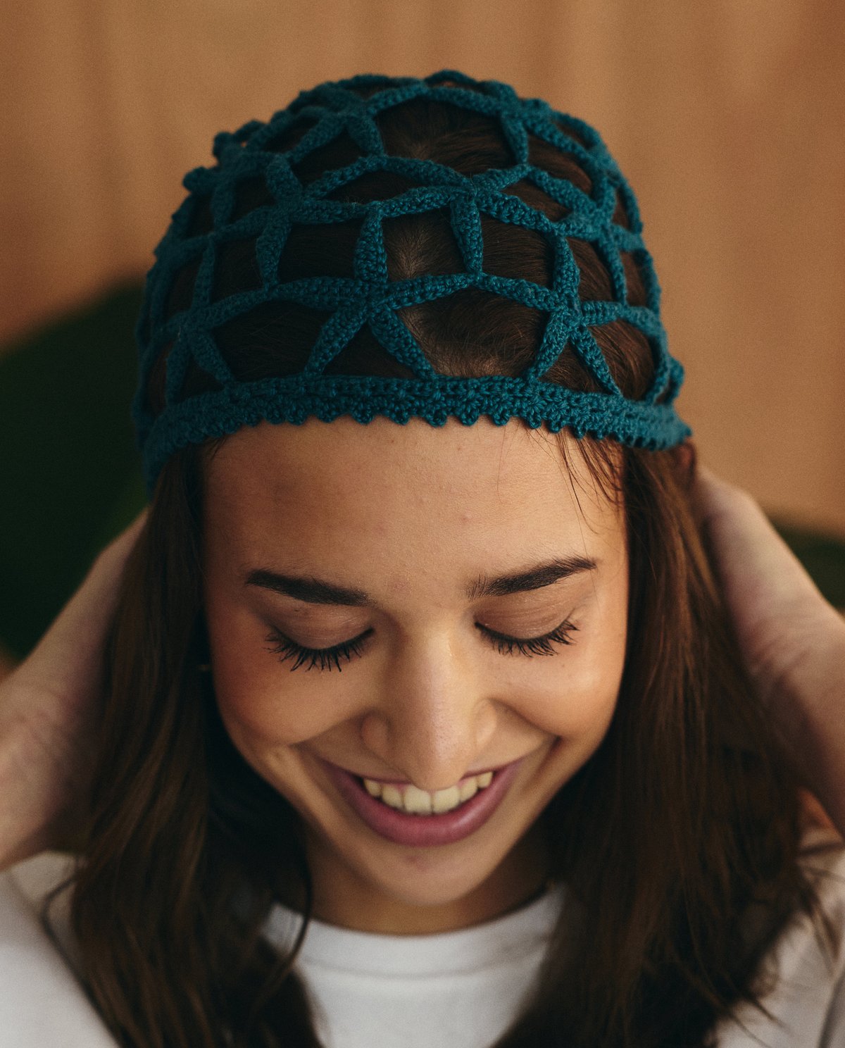 Mulher com touca de crochê azul-petróleo sorrindo e olhando para baixo