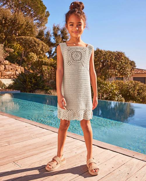 Menina com vestido de crochê cinza claro e sandálias bege junto a piscina ao ar livre