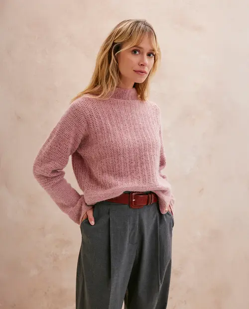 Mulher com camisola rosa e calças cinza em fundo bege