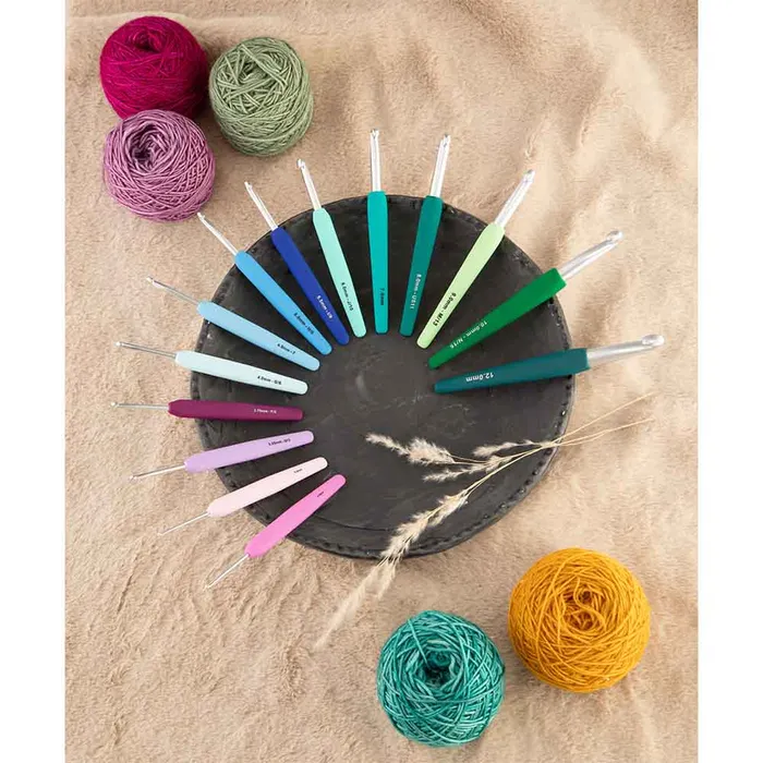 Agulhas de crochet coloridas em círculo com novelos de lã numa superfície bege