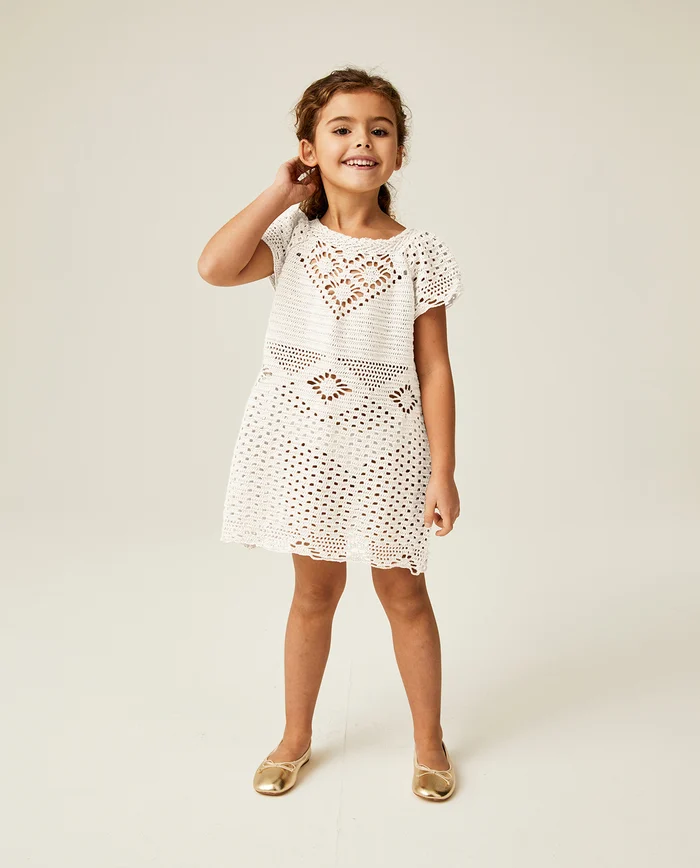 Menina com vestido branco de crochê e sapatilhas douradas