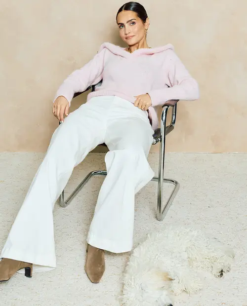 Mulher com roupa casual sentada numa cadeira de metal com um cão branco no chão
