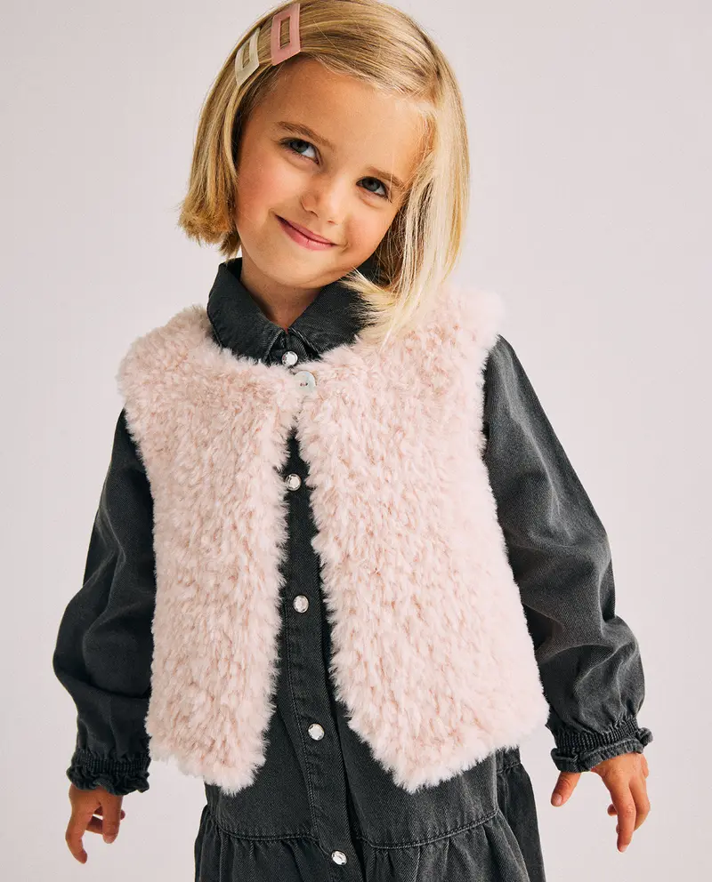 Menina com vestido preto e colete peludo rosa claro numa pose sorridente