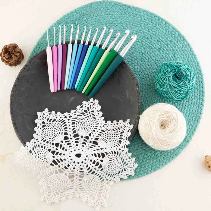 Conjunto de agulhas de crochet coloridas sobre prato cinzento com bola de fios e trabalho de crochet branco