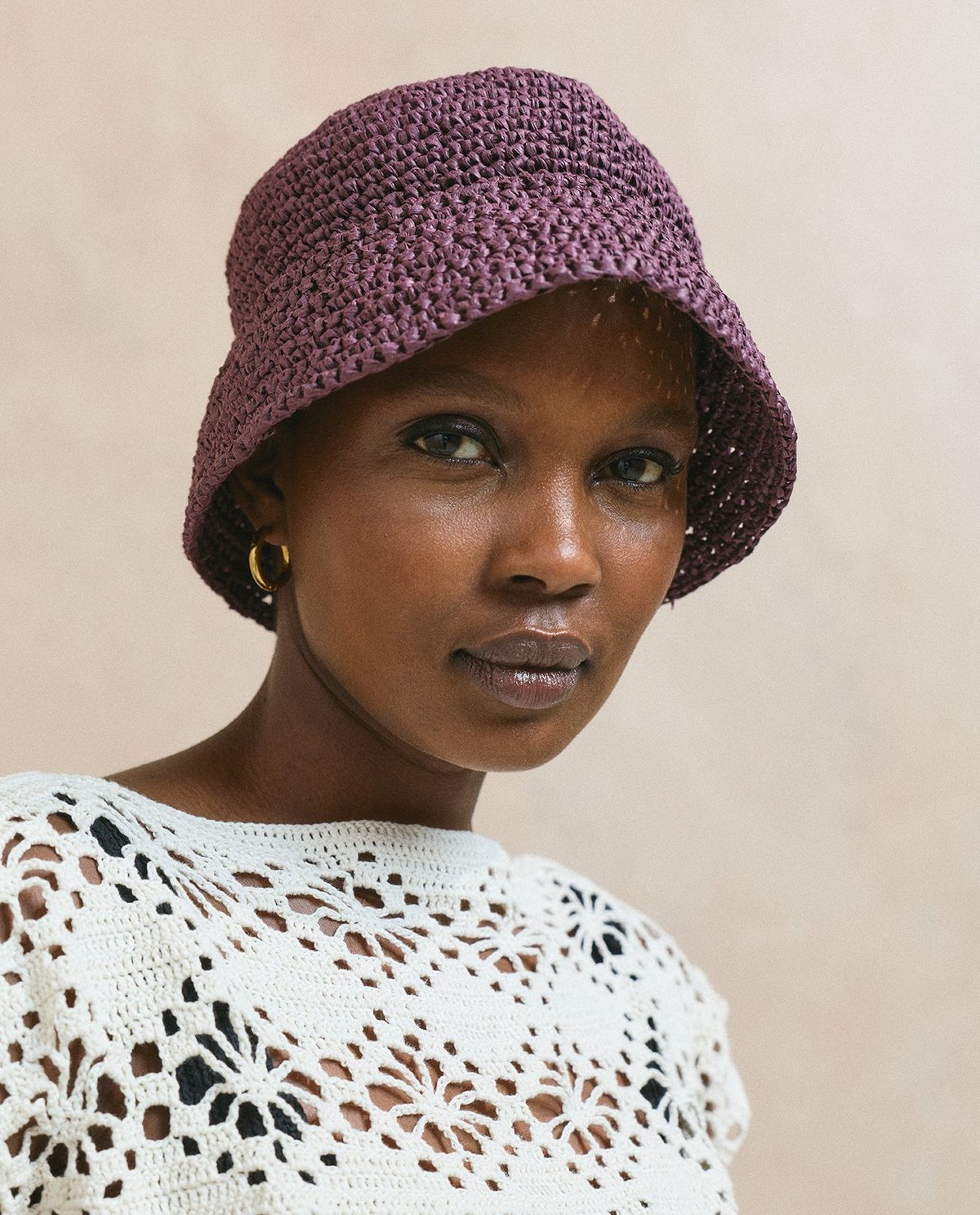 Mulher usando chapéu bucket roxo trançado e blusa de croché branca