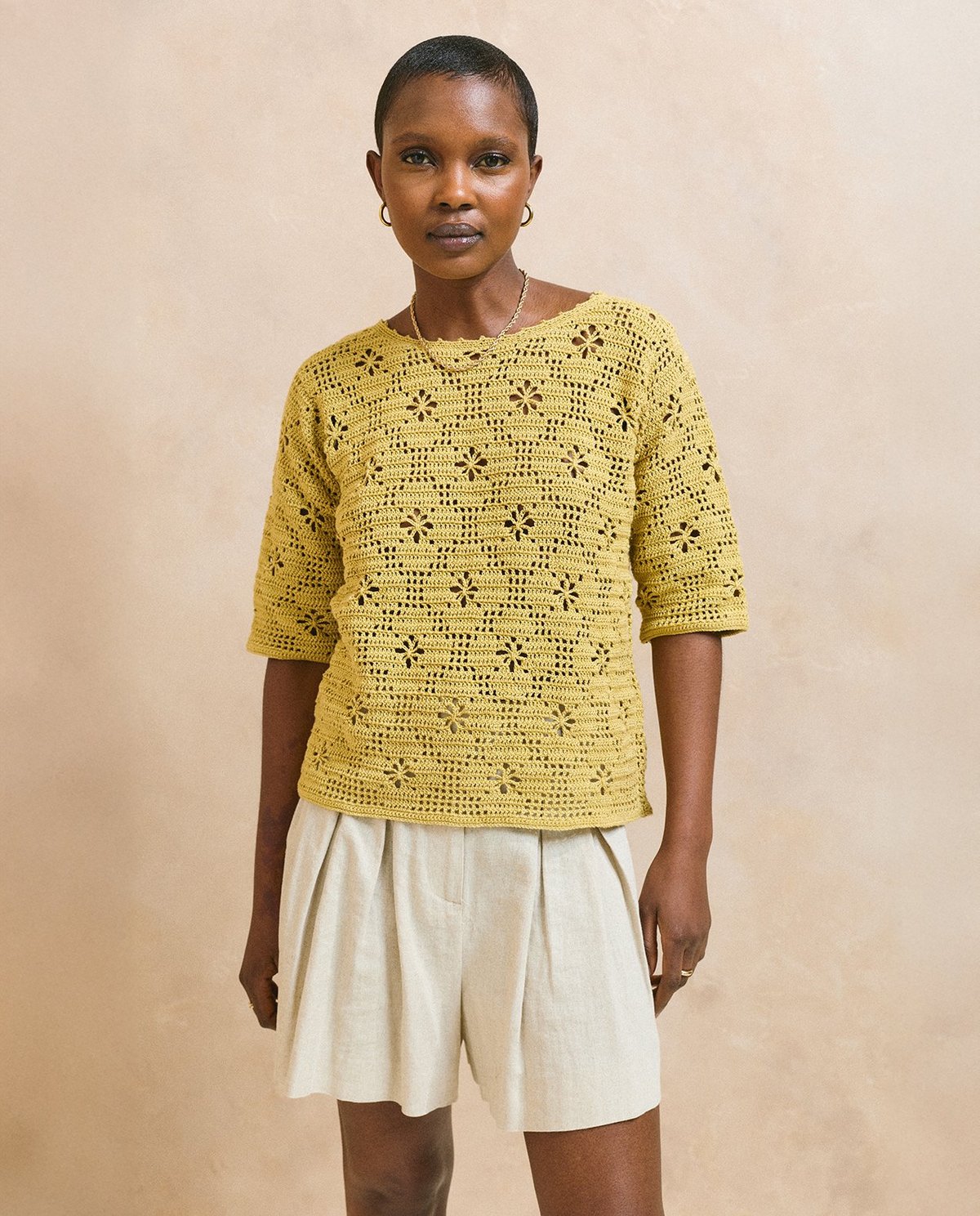 Mulher com camisola amarela em crochet e calções brancos