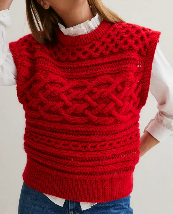 Colete vermelho trançado sobre camisa branca e calça azul