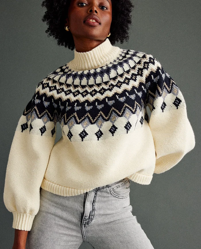Camisola de malha creme com padrão geométrico colorido e jeans cinzentos