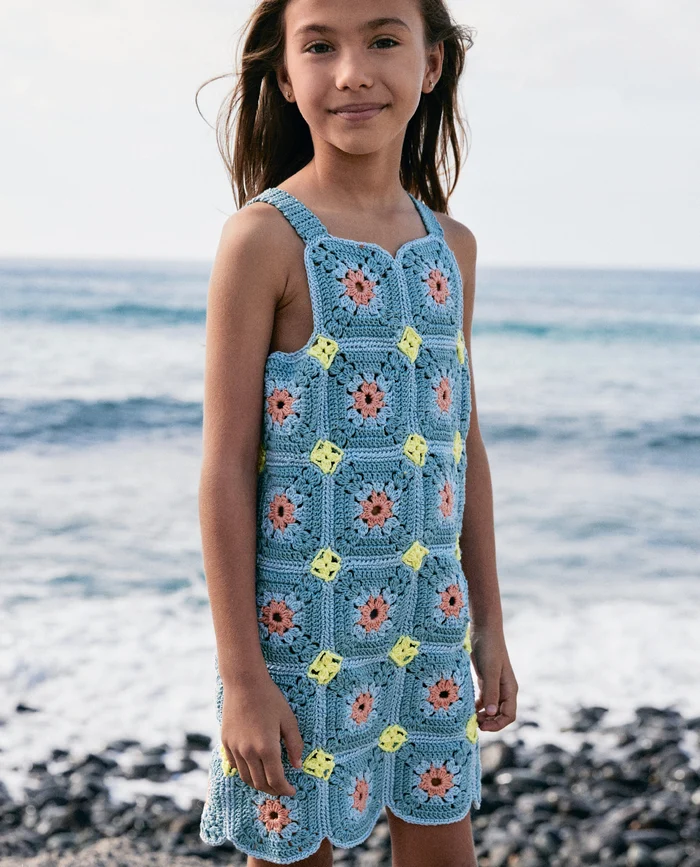 Menina com vestido de crochet colorido à beira-mar.