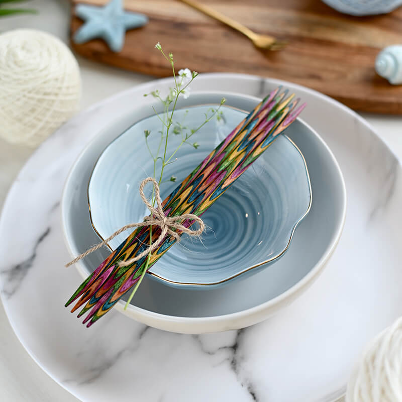 Conjunto de pratos e tigela de porcelana com pauzinhos de madeira coloridos e flor sobre prato marmoreado