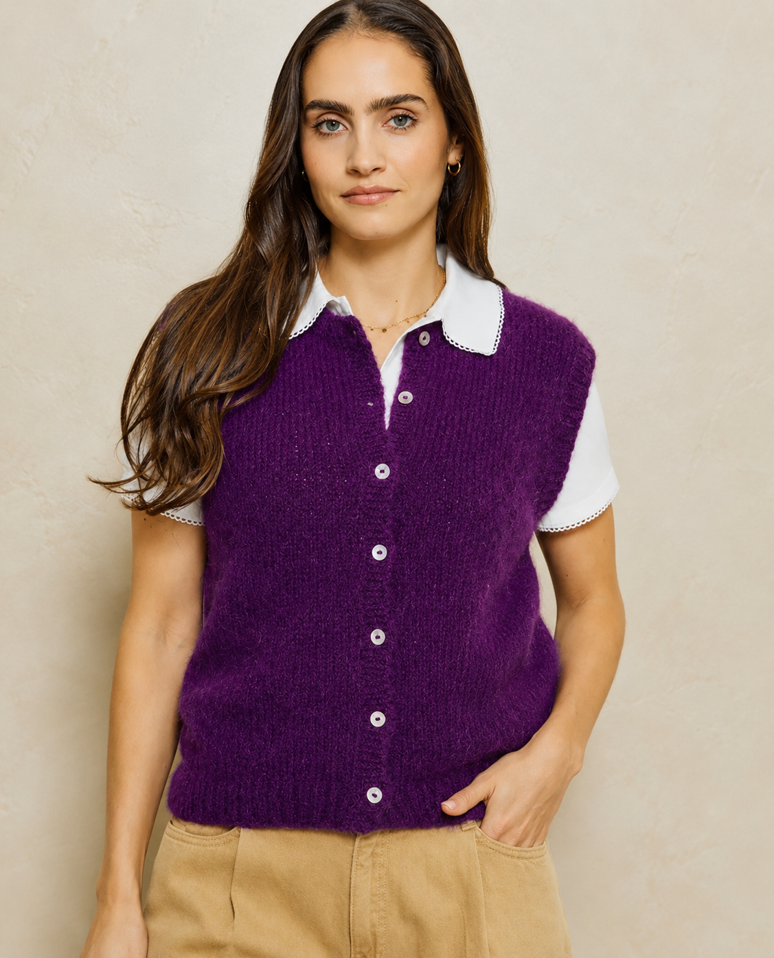 Mulher a usar colete roxo de malha com botões sobre camisa branca e calças bege