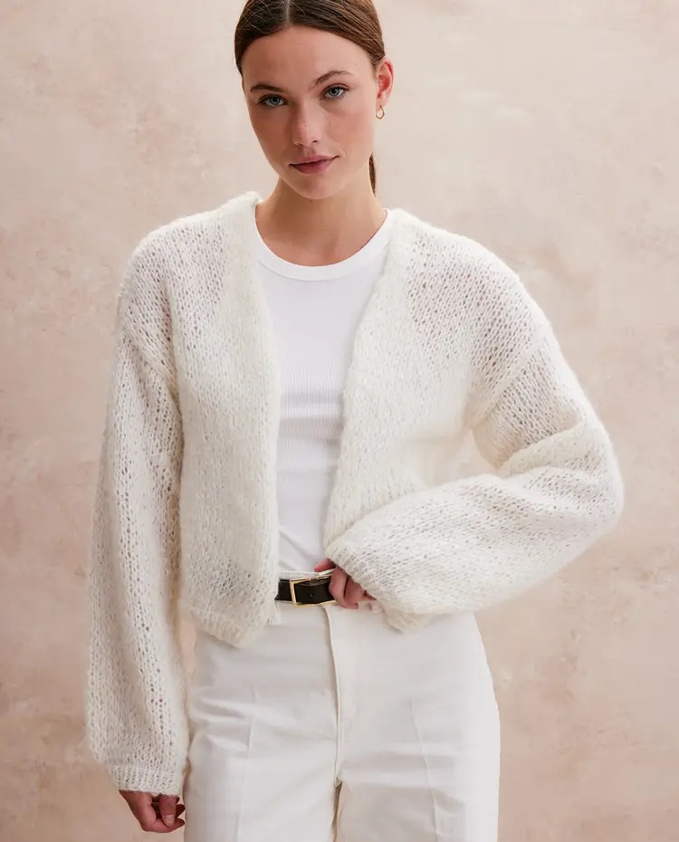 Cardigan branco bege claro de malha grossa aberto, com t-shirt e calças brancas.