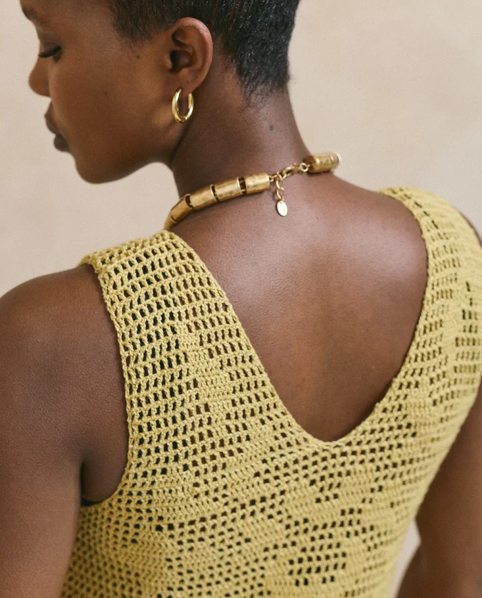 Mulher de costas a usar vestido amarelo de croché e colar dourado segmentado