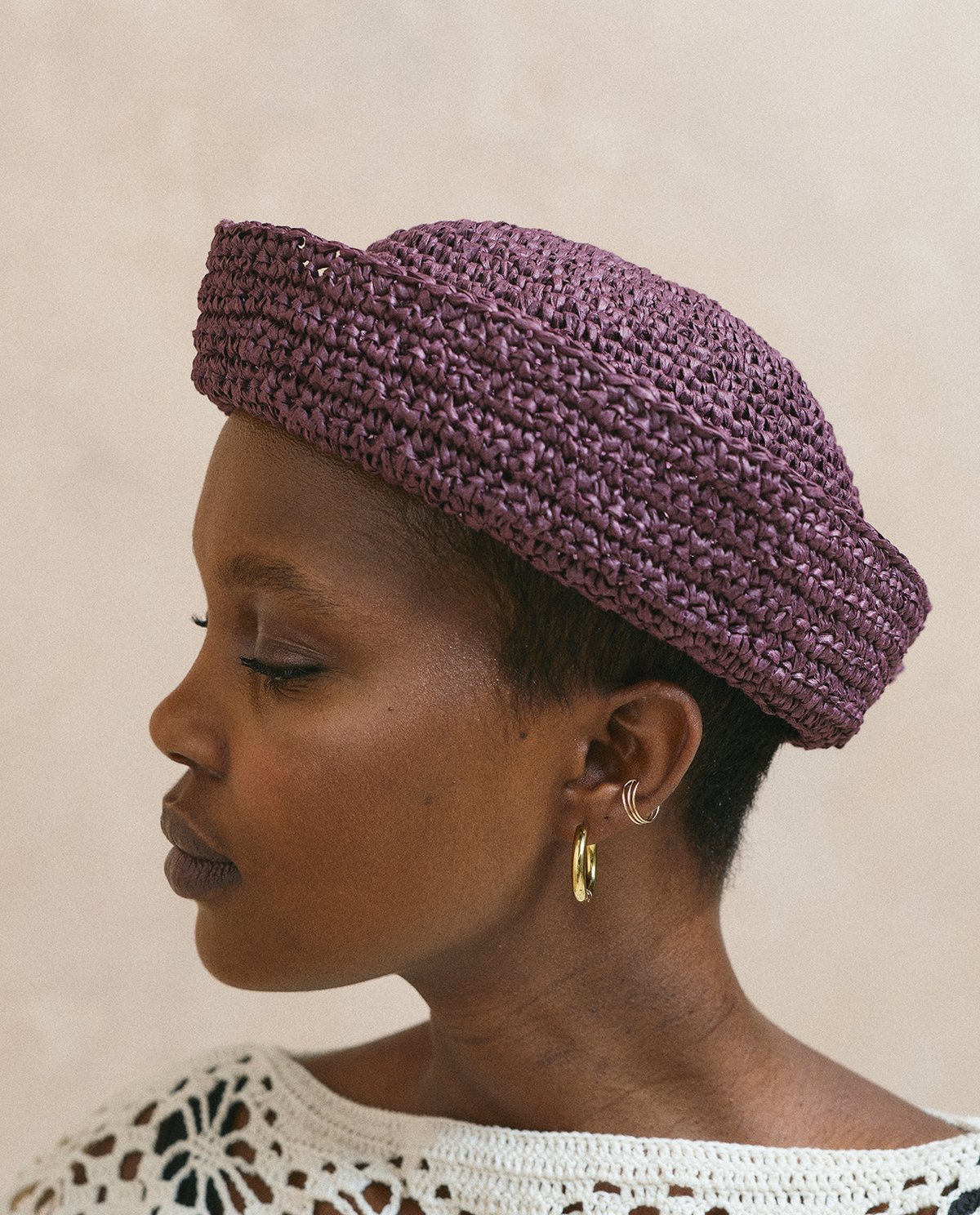 Mulher de perfil com chapéu roxo de tricô e brincos dourado e prata.