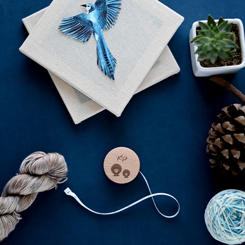 Quadros de tela com pássaro azul, carretel de madeira com texto KP, planta suculenta, pinha, novelo e fio sobre fundo azul