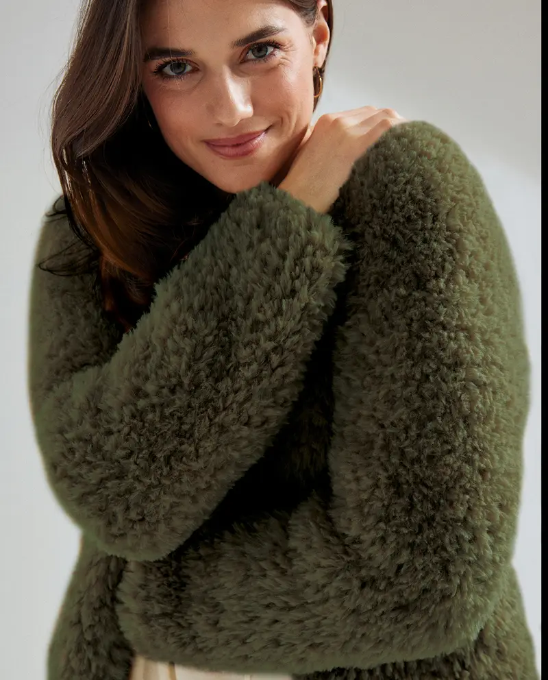 Pessoa com casaco verde felpudo em fundo neutro