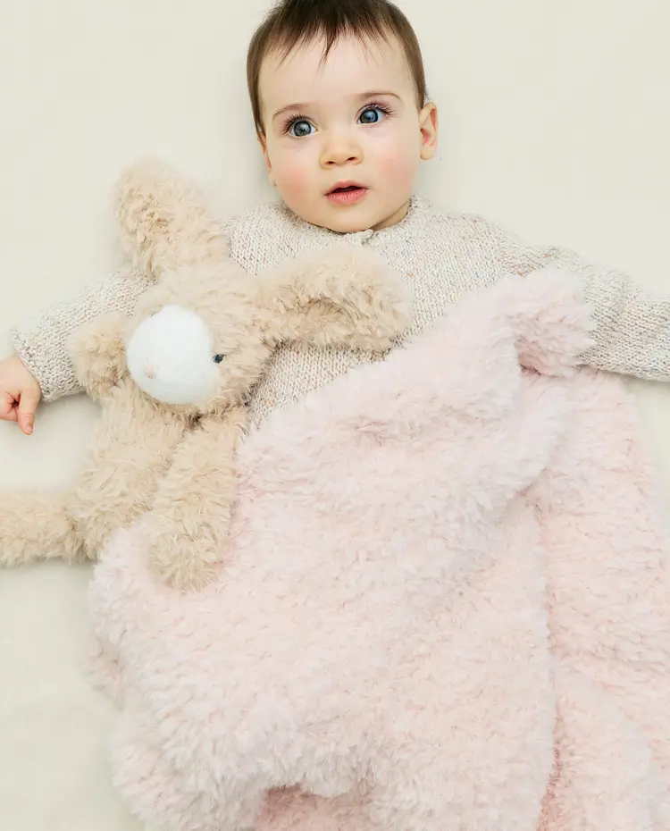 Bebé com camisola bege de malha, manta cor-de-rosa felpuda e peluche de coelho bege