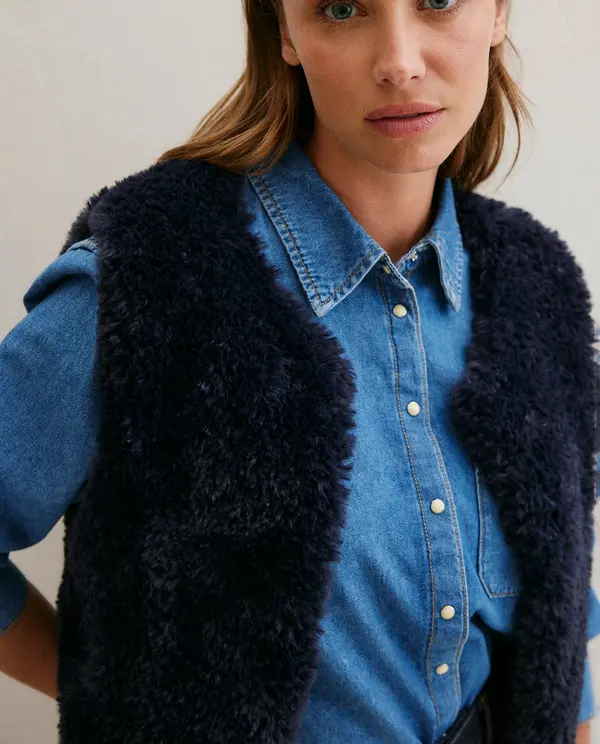 Colete preto peludo sobre camisa jeans azul com botões