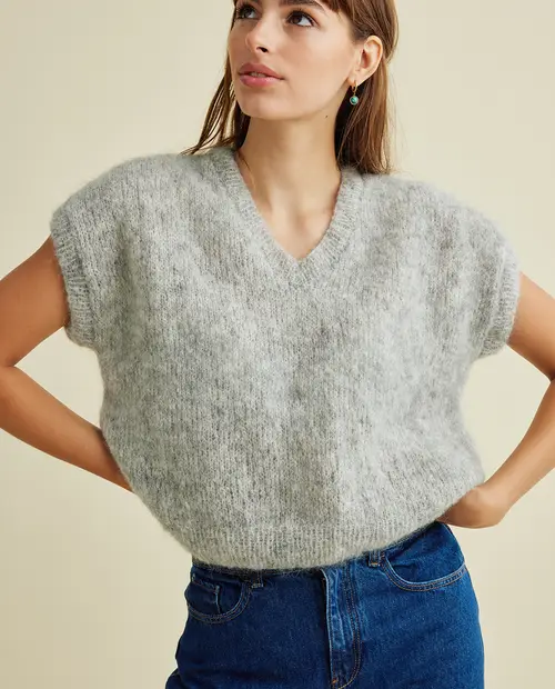 Camisola cinzenta de malha com decote em V e mangas curtas largas, calças de ganga azuis numa mulher