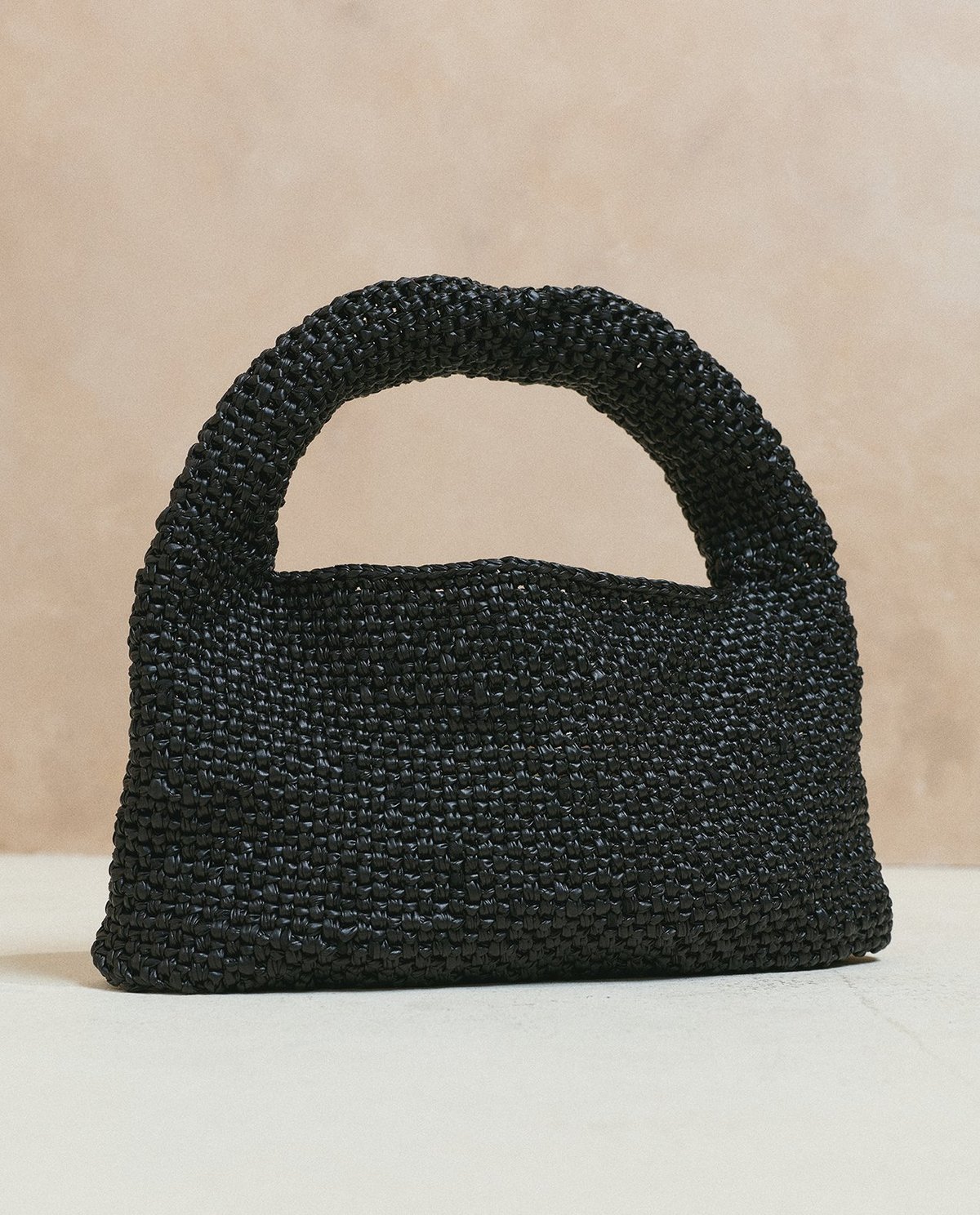 Mala de mão preta tecida com alça integrada sobre superfície clara