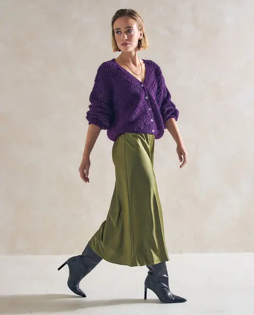 Mulher jovem com casaco roxo, saia verde e botas pretas