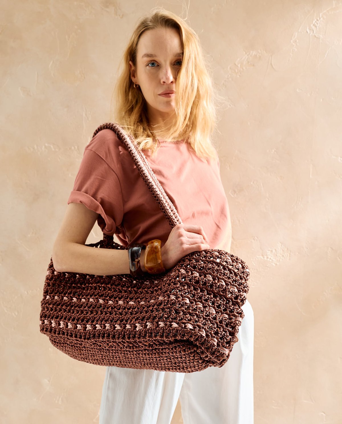 Mulher com mala de crochê castanha e roupa clara