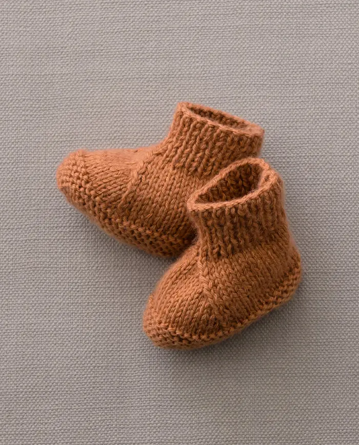Botins de lã castanha tricotada para bebé sobre fundo cinzento claro