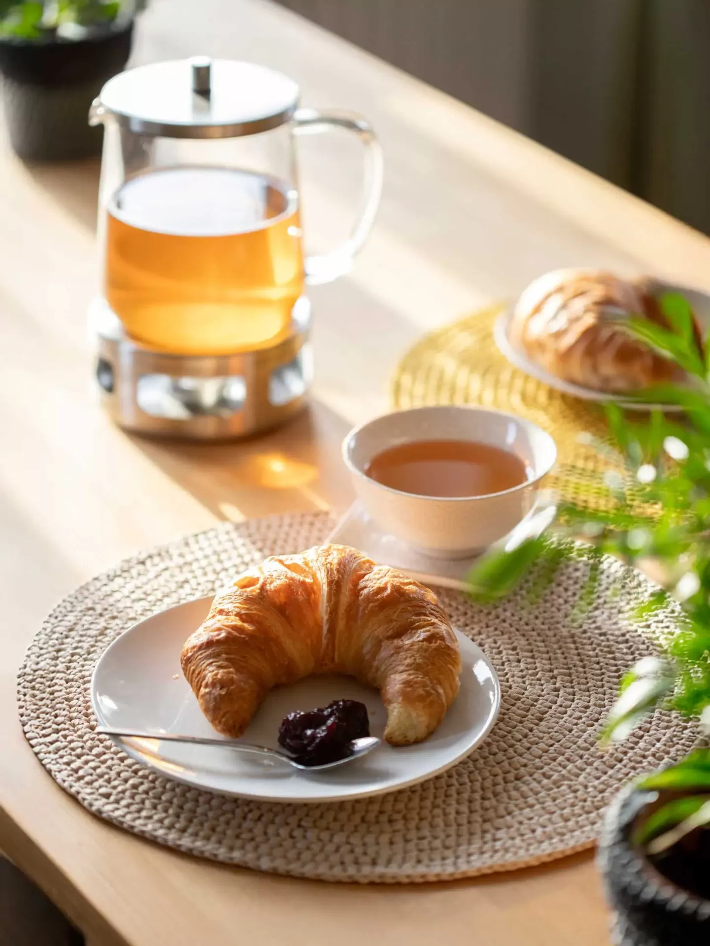 Bule de chá, chávena, croissant com compota e colher sobre mesa de madeira e base de tecido