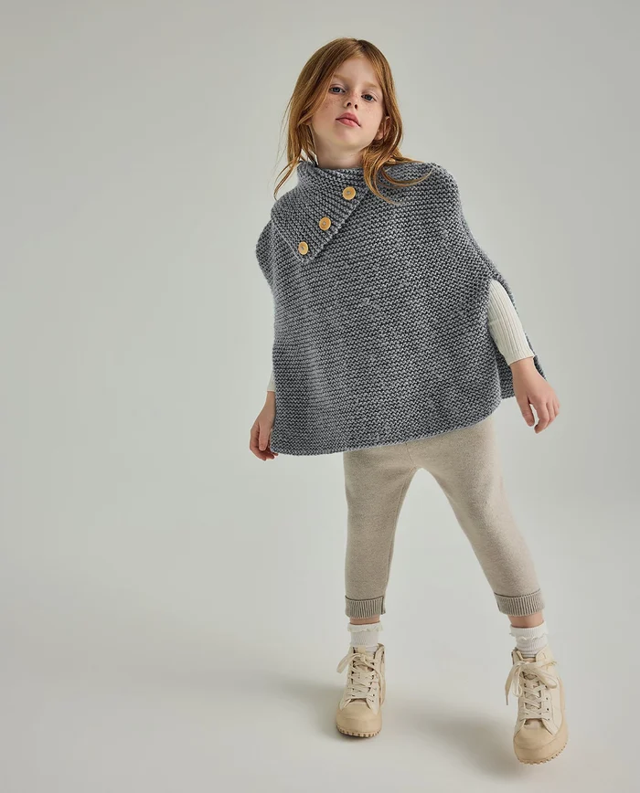 Menina com poncho cinzento, calças bege e botas bege