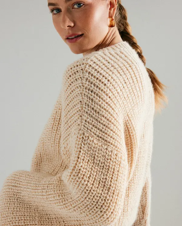 Mulher com camisola creme de malha grossa e cabelo apanhado