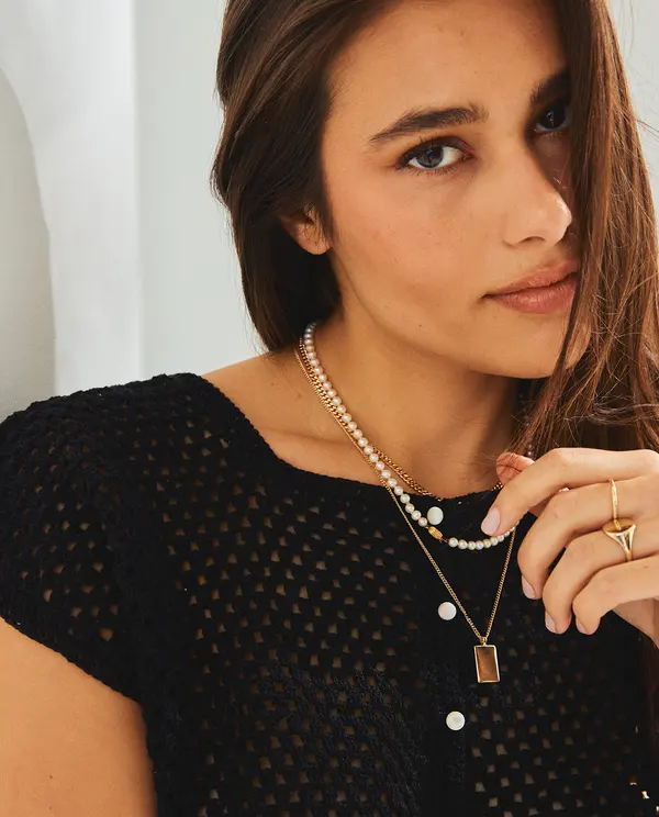 Colares dourado e de contas brancas usados com suéter preto de malha