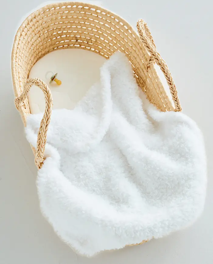 Cesto de vime natural com tecido branco felpudo e um biberão amarelo ao lado
