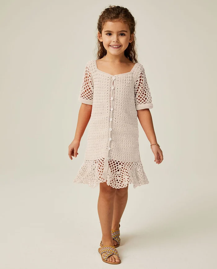 Menina com vestido de crochet bege e sandálias coloridas