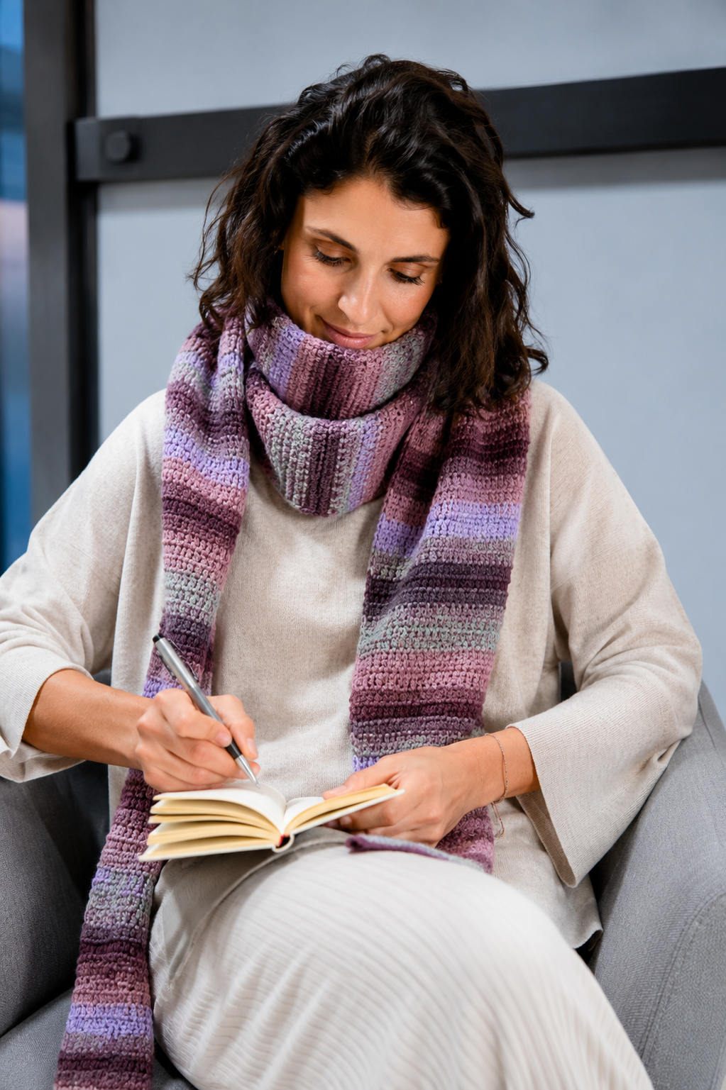 Mulher a escrever num caderno com uma echarpe de lã colorida e camisola bege
