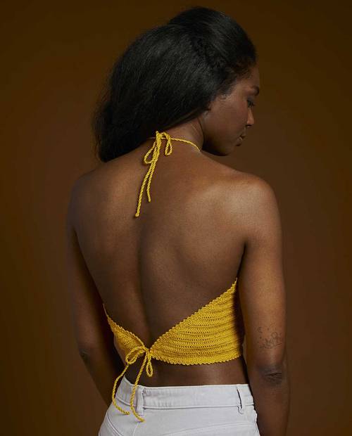 Mulher vista de costas a usar top amarelo de crochet com fecho de laço e calças brancas