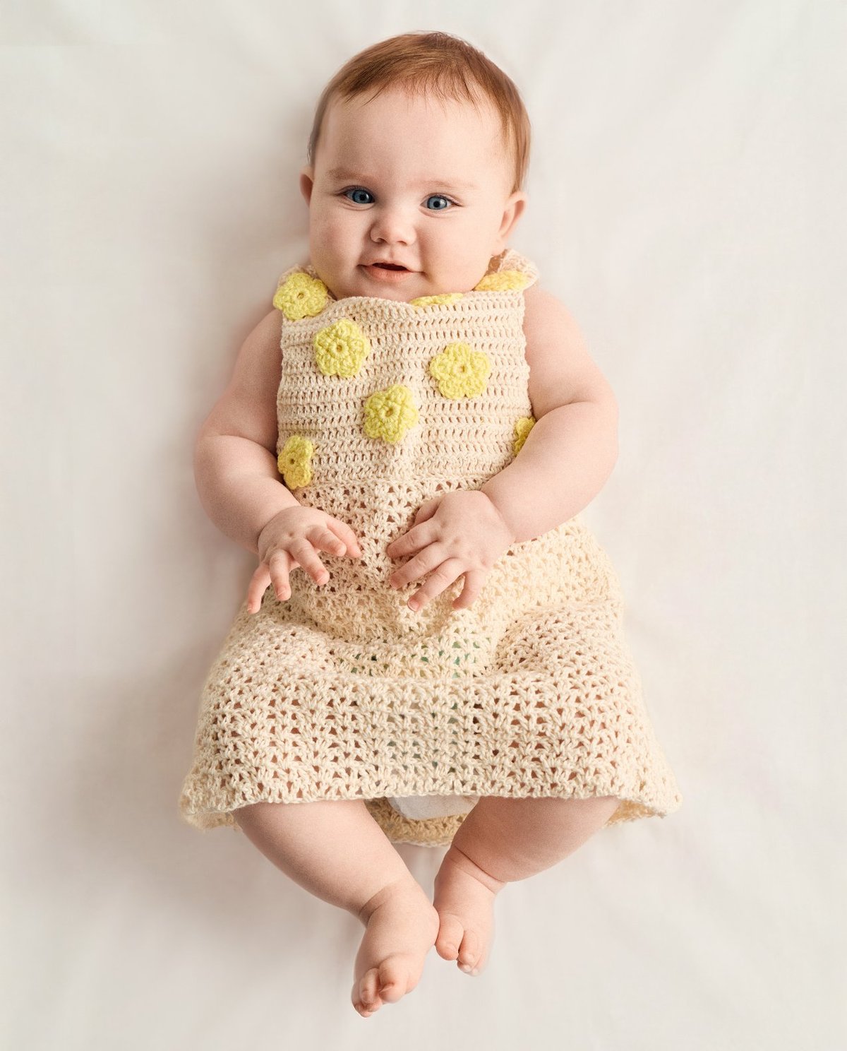 Bebé com vestido de malha bege com flores amarelas em relevo