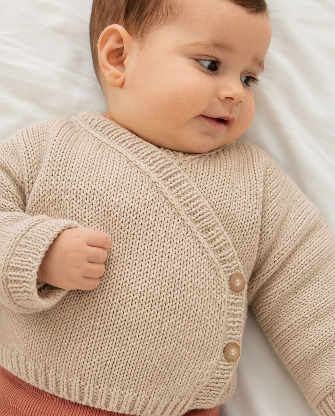 Bebé com camisola de malha bege e calças cor de tijolo deitado