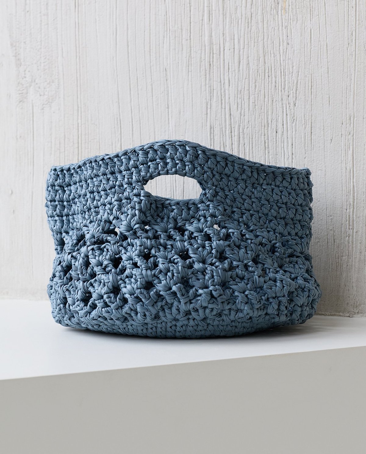 Bolsa azul trançada com alça integrada e abertura oval em superfície branca