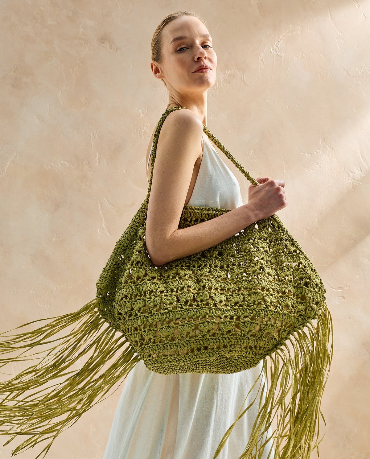 Mulher com vestido branco e mala verde trançada com franjas