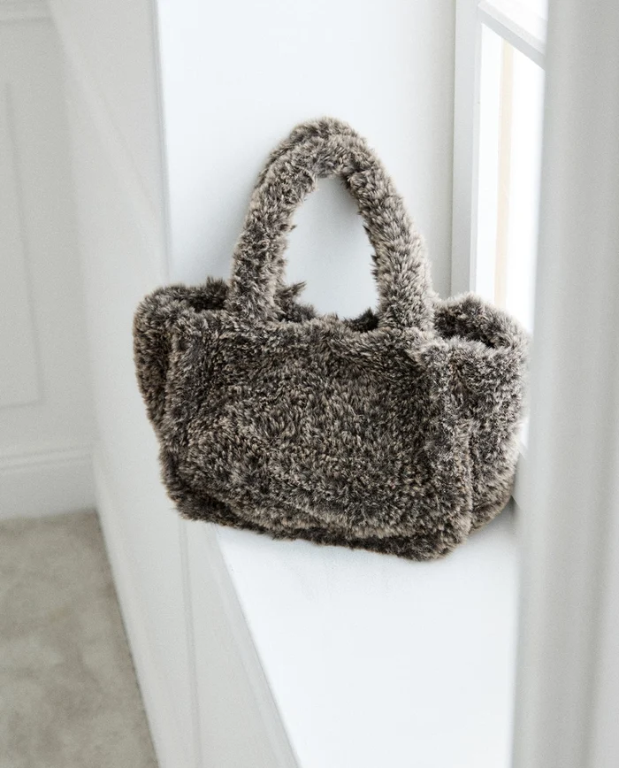 Bolsa de mão peluda cinzenta numa janela branca