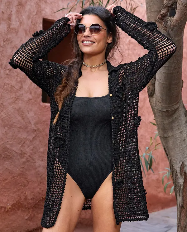 Mulher com camisola de malha preta e fato de banho preto ao ar livre