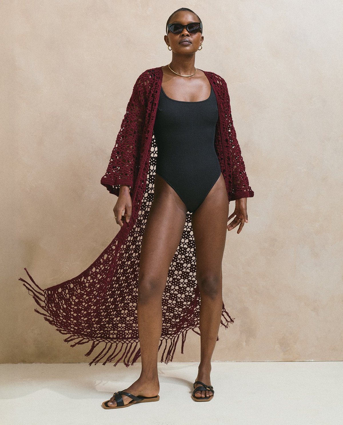 Mulher com fato de banho preto e casaco de crochet vermelho vinho com franjas