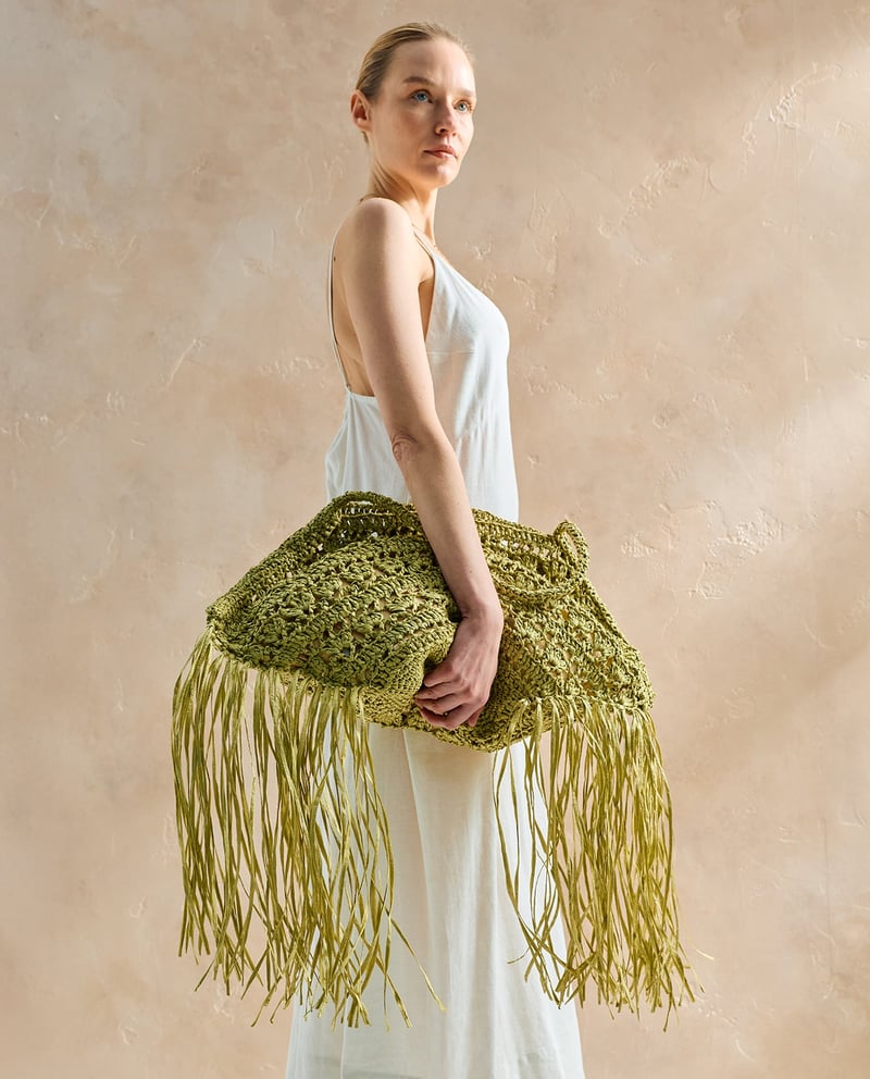 Mulher com vestido branco segurando bolsa verde de crochê com franjas