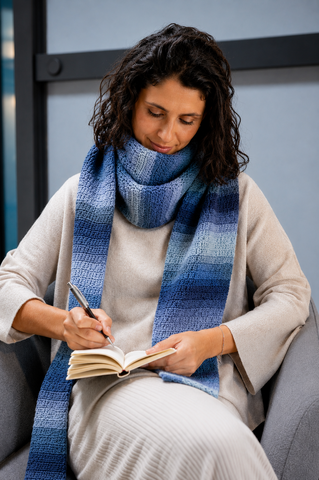 Mulher sentada com cachecol azul e escrevendo num caderno